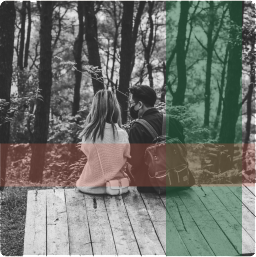 Couple seated on lakeside deck, backs to camera, enjoying forest view