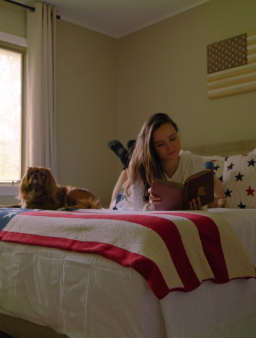 Guest reading on queen-size bed with patriotic throw and spaniel