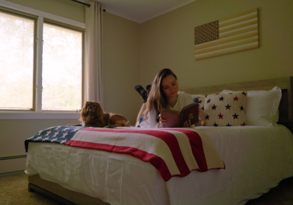 Guest reading on queen-size bed with patriotic throw and spaniel